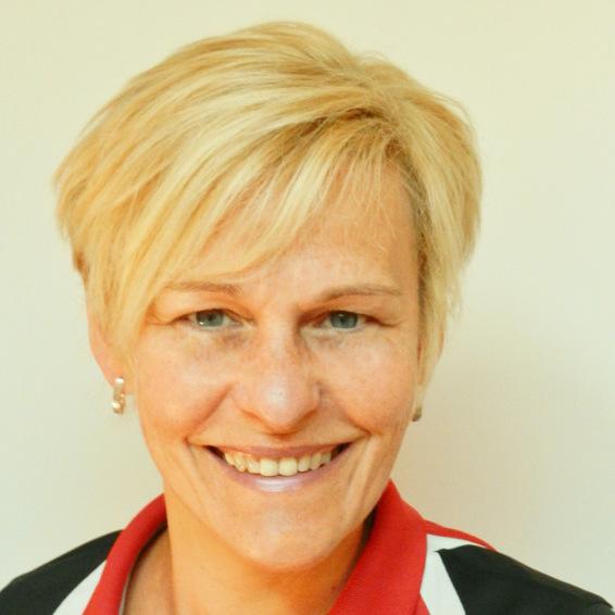 Porträt einer lächelnden Frau mit blonden Haaren, die ein schwarz-rotes Oberteil trägt, vor einem hellen Hintergrund.