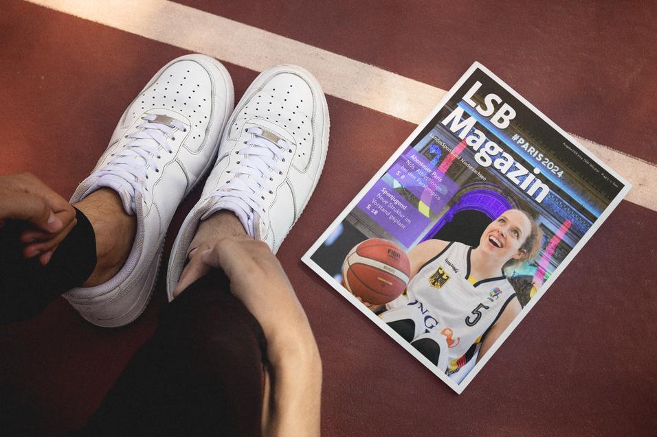 Wei&szlig;e Sneakers stehen neben einem LSB Magazin, das auf einem Basketballfeld liegt.