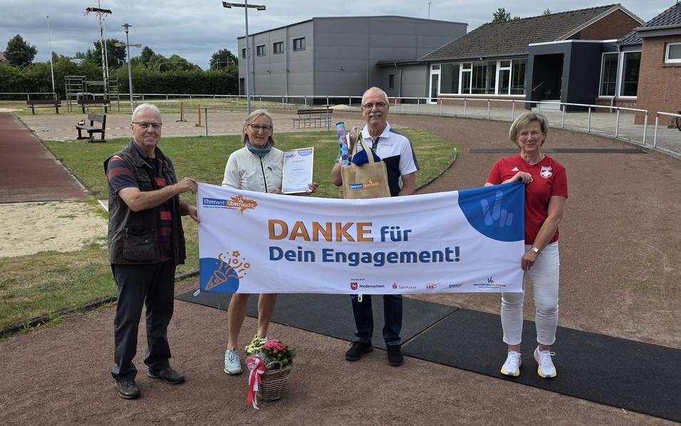 Gruppe von vier Personen hält ein Banner mit der Aufschrift „DANKE für Dein Engagement!“ auf einem Sportplatz.