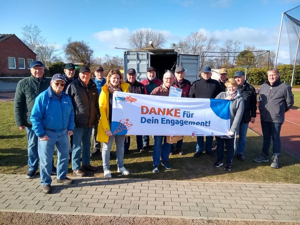 Gruppe von 15 Personen in Outdoor-Kleidung hält ein Banner mit der Aufschrift „DANKE für Dein Engagement!“