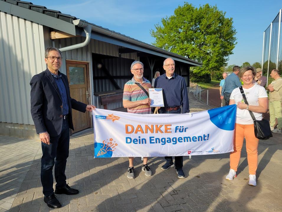 Gruppenszene mit vier Personen, die ein Banner mit der Aufschrift „DANKE für Dein Engagement!“ halten.