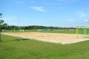 Sandplatz f&uuml;r Beachvolleyball mit zwei Netzen, umgeben von Rasen und Fu&szlig;balltoren auf einem Sportgel&auml;nde.