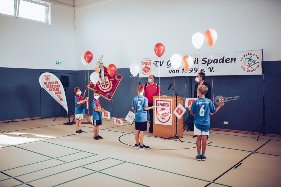 Grupp von Kindern in blauen Trikots h&auml;lt Schilder und steht vor einer B&uuml;hne mit Luftballons und Vereinsbanner.