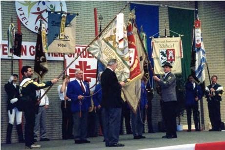 Eine Gruppe von Personen h&auml;lt Fahnen w&auml;hrend einer Zeremonie in einer Halle, Umgeben von dekorativen Bannern an der Wand.