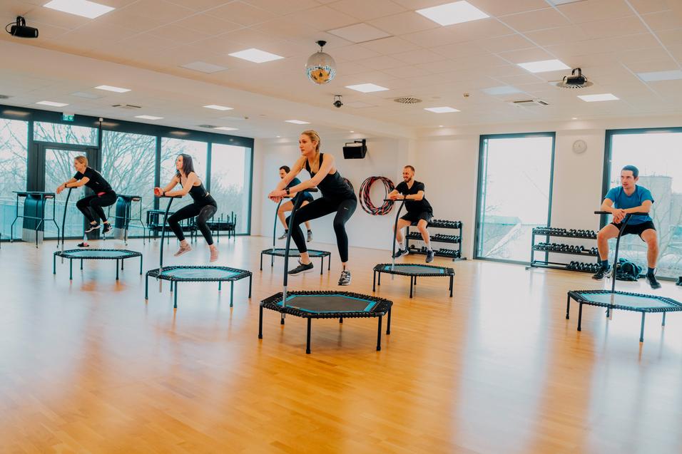Gruppe von Menschen beim Trampolinspringen in einem modernen Fitnessraum mit großen Fenstern.