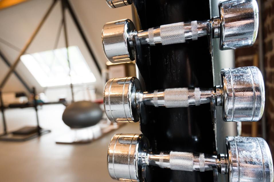 Nahaufnahme von mehreren chromierten Hanteln an einem Ständer in einem modernen Fitnessstudio.